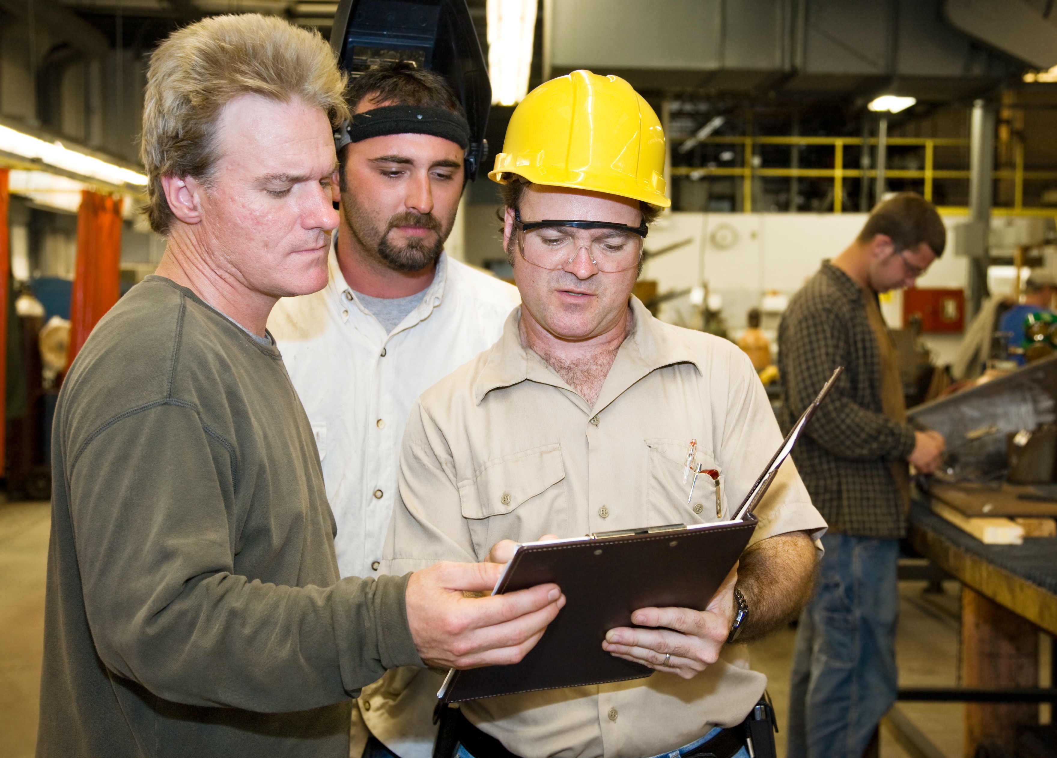 An OSHA inspector and two factory workers looking at a clipboard