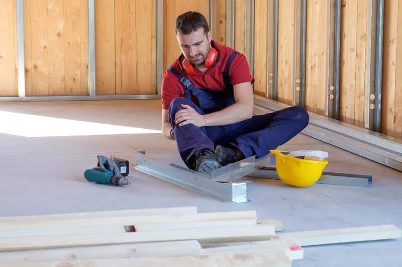 What is a work-related injury? Construction worker clutches knee at a building site.