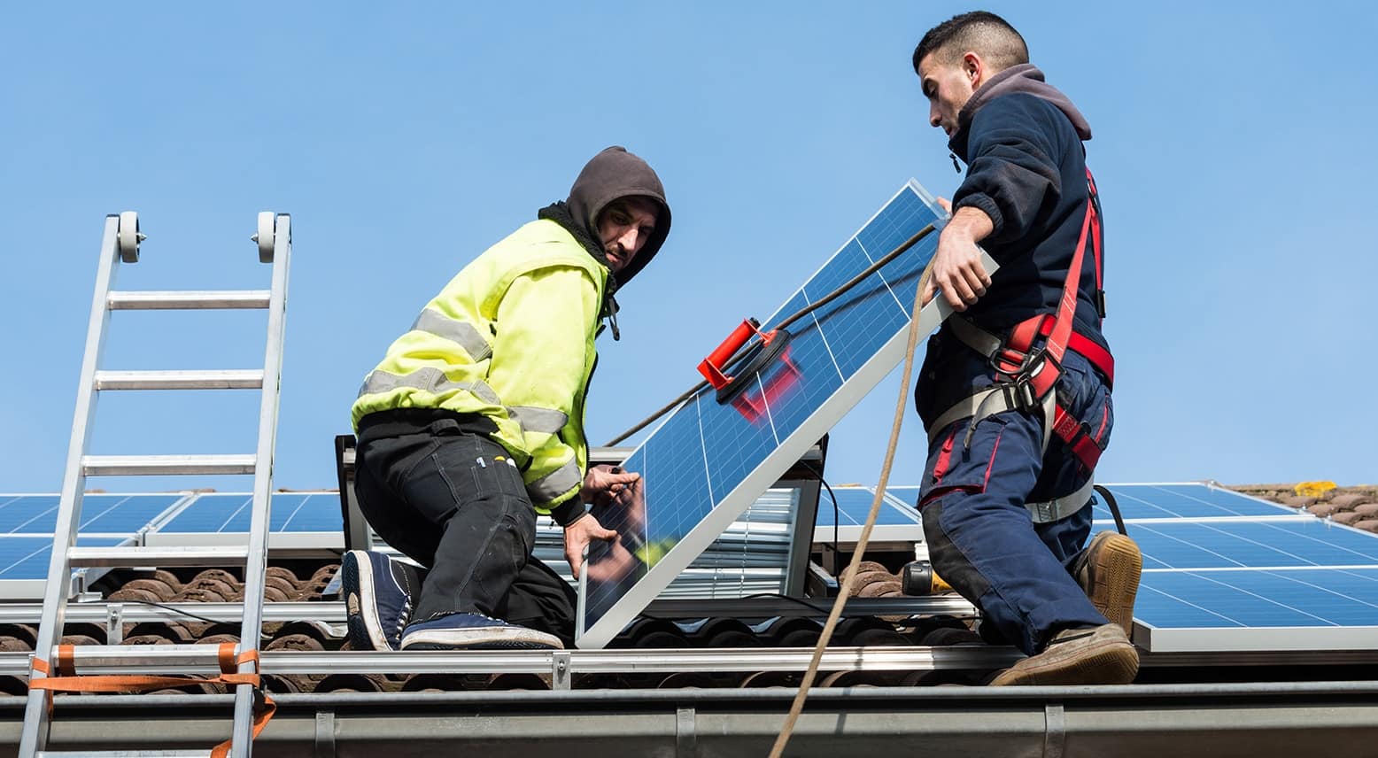 two men carrying solar panel on roof