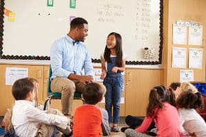 Schoolgirl at front of elementary class talking with teacher