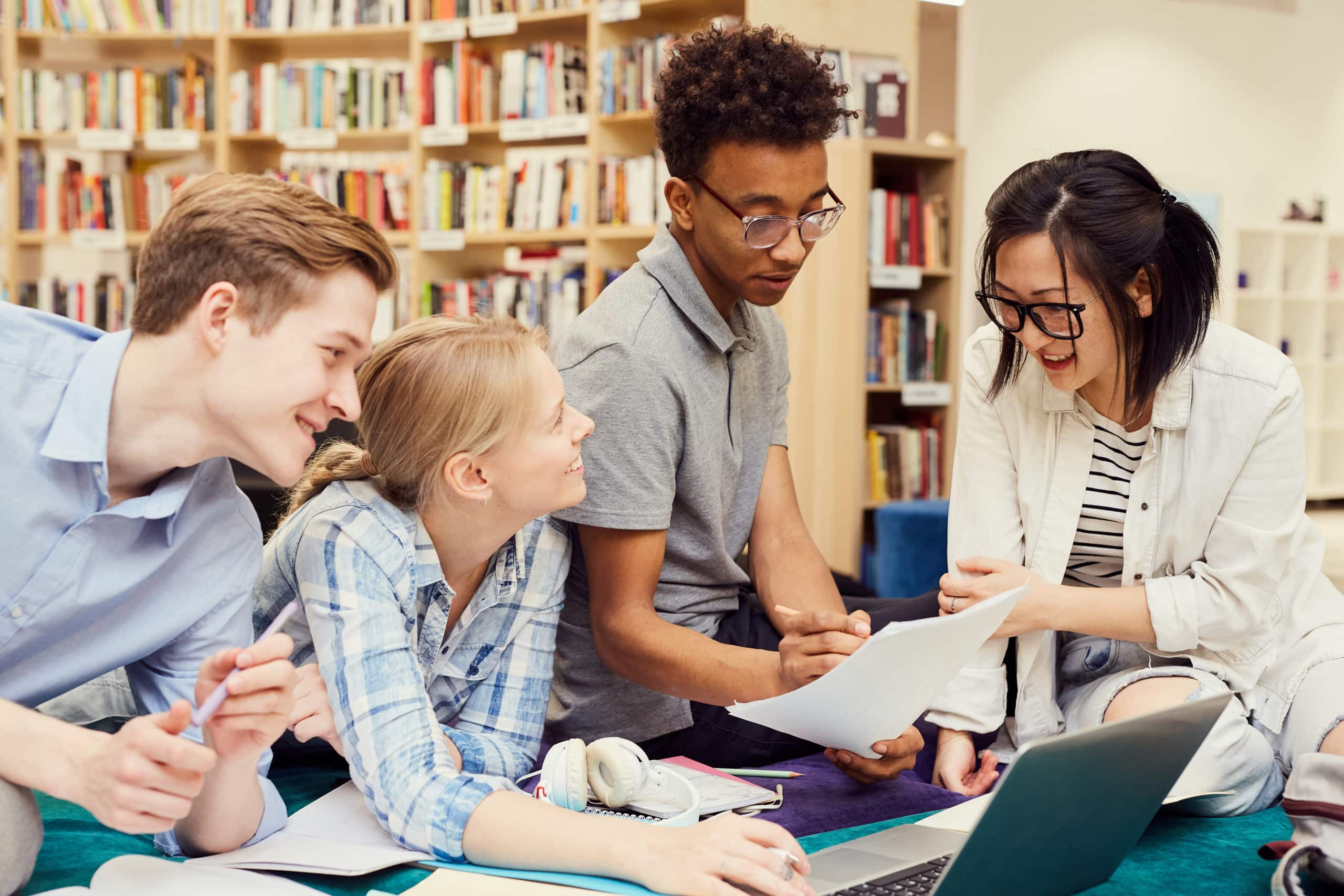 positive young multi-ethnic students sitting in modern library