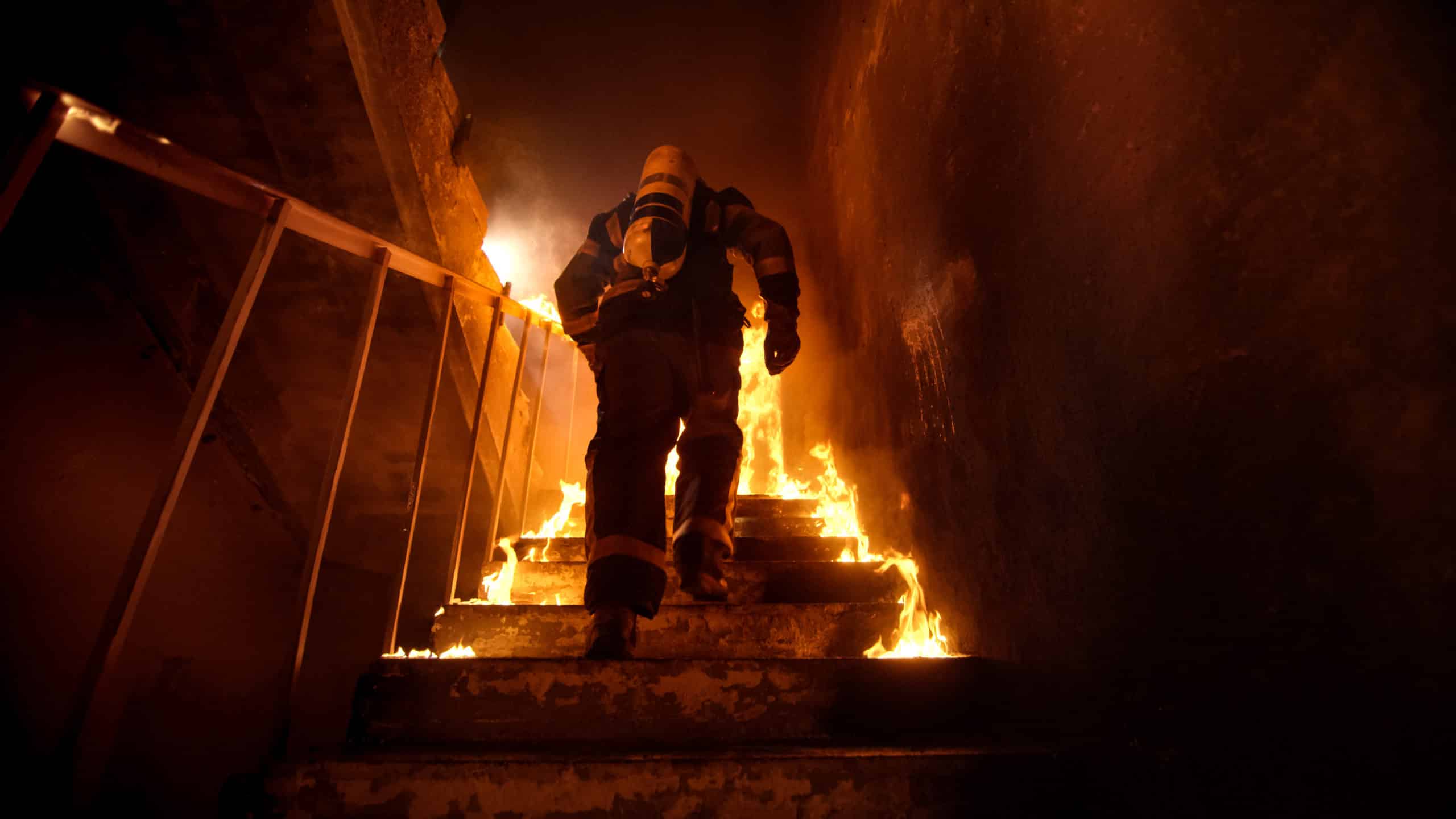Firefighter climbing up stairs in a structure fire