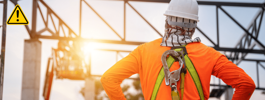 A construction worker with a safety harness on looks at the job site