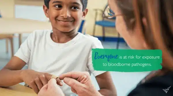 Teacher helps apply a bandaid to a cut on a young boy’s finger. Text says "Everyone is at risk for exposure to bloodborne pathogens."