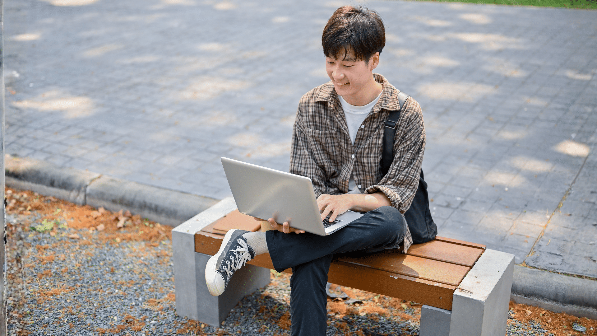 University student work on a laptop, sitting outside on a bench.