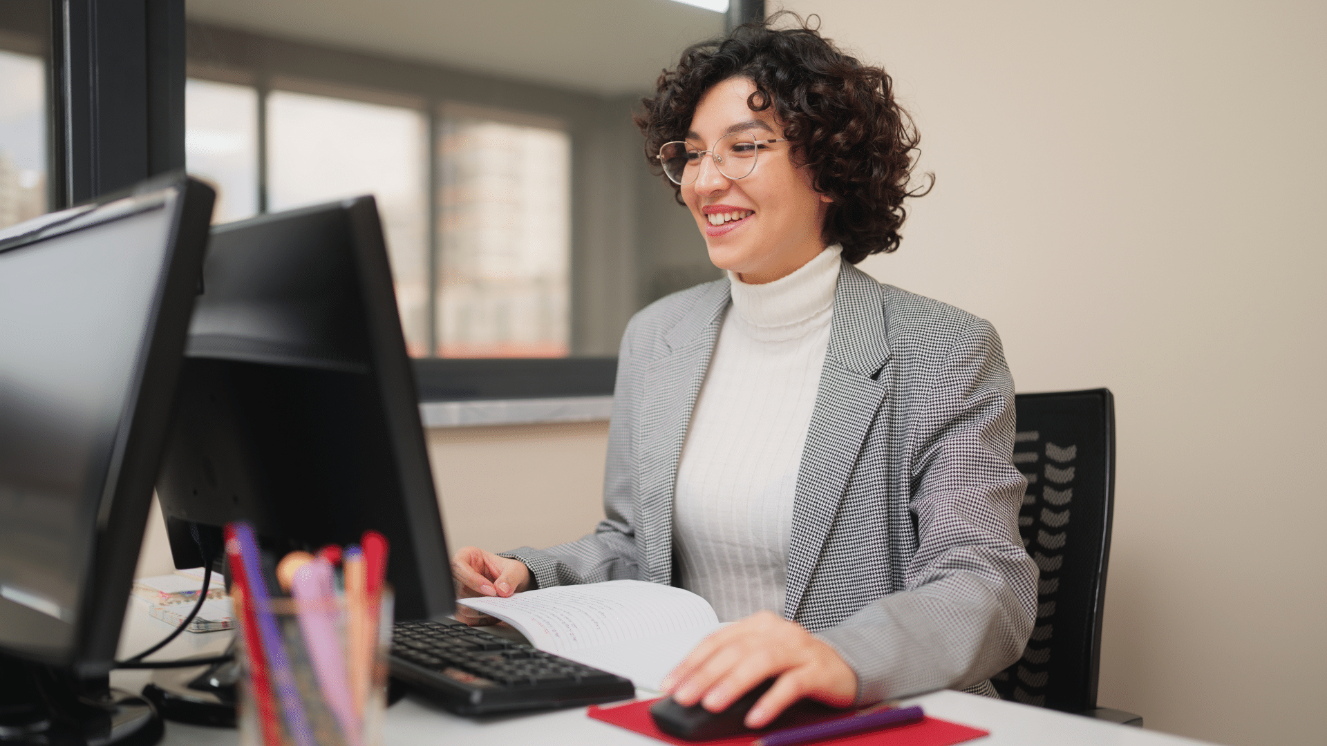 A k-12 staff member smiling at her computer while sitting at a desk.