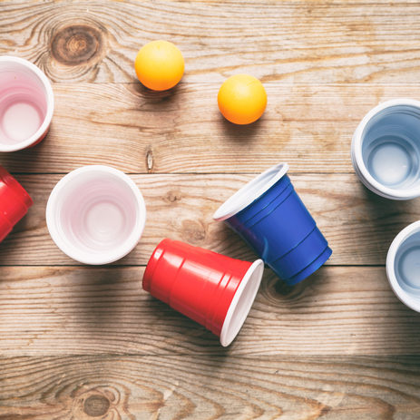 Beer pong, college party game. Plastic red and blue color cups and ping pong balls on wooden background, top view